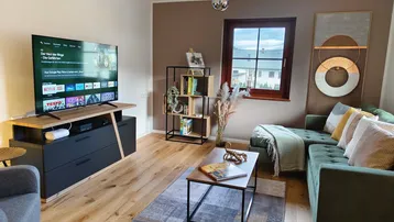 Modernes Wohnzimmer mit großem Fernseher, bequemer Couch und Holzboden.