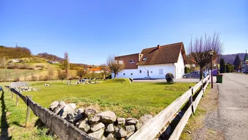 Ländliche Ansicht des Hauses mit großem Rasenbereich und Holzzaun im Vordergrund.