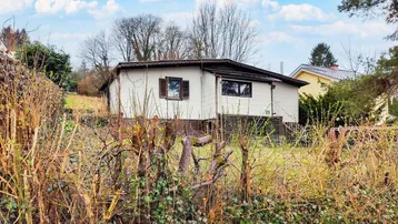 Älteres Einfamilienhaus mit weißer Fassade und dunklem Dach, umgeben von winterlicher Vegetation.