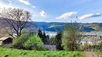 Landschaftsblick mit See, Bergen und grüner Vegetation unter blauem Himmel und Wolken.