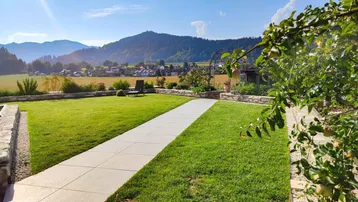 Gepflegter Rasenbereich im Garten mit gepflastertem Weg und Bergblick.