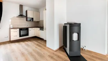 Offener Wohnbereich mit integrierter Küche, modernem Ofen und hellem Laminatboden.