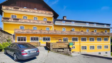 Traditionelles gelbes Gebäude mit mehreren Balkonen und einem geparkten Auto davor unter blauem Himmel.