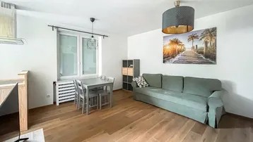 Helles Wohn- und Esszimmer mit Parkettboden, bequemer Couch und Essbereich für vier Personen.