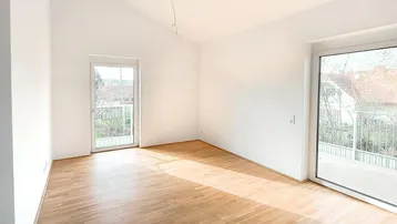 Heller Raum mit Parkettboden, schräger Decke und Zugang zu einem Balkon, durchflutet von natürlichem Licht.