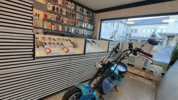 Innenansicht eines modernen Handy-Shops mit Auslagen für Zubehör und einem Roller als Dekoration im Vordergrund.