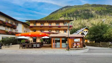 Ansicht des Gebäudes "Mallnitz Appartements" mit Außenterrasse, umgeben von Bergen und grüner Landschaft.