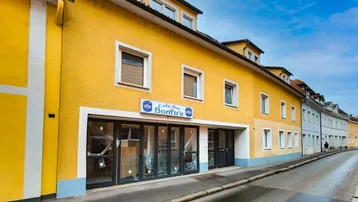 Lange gelbe Fassade eines Gebäudes mit einer Café-Bar im Erdgeschoss und Fenstern in den oberen Etagen.