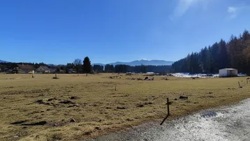 Weitläufige Landschaft mit Wiesen, Wäldern und Bergen unter strahlend blauem Himmel.