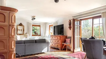 Gemütlicher Wohn-Essbereich mit traditionellem Kachelofen, Holzboden und Zugang zum Balkon.