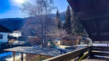 Sonniger Balkon mit Sitzgelegenheiten und Blick auf die umliegende Berglandschaft.