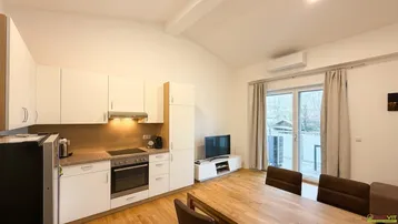 Heller offener Wohn-Essbereich mit integrierter Küche, Holzboden und Zugang zum Balkon.