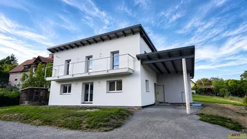 Modernes Einfamilienhaus mit weißer Fassade, Balkon und Carport unter blauem Himmel.