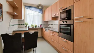 Funktionale Küche mit Holzschränken, Einbaugeräten und einem kleinen Essbereich am Fenster.