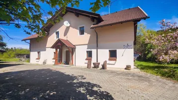 Traditionelles Haus mit gepflastertem Vorplatz und grüner Umgebung unter blauem Himmel.