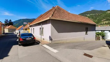 Gebäudeansicht von außen an einer Straßenecke mit Bergen im Hintergrund unter blauem Himmel.