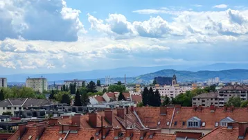 Weitläufiger Blick über die Dächer der Stadt und die umliegende Berglandschaft bei Tag.