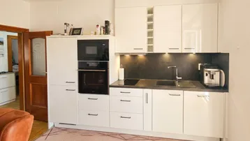 Moderne Einbauküche mit weißen Hochglanzfronten, integriertem Backofen und Mikrowelle sowie dunkler Arbeitsplatte.