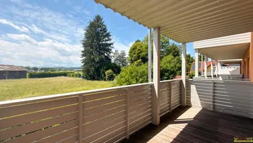 Geräumiger Balkon mit Holzboden und weitem Blick ins Grüne und die Landschaft.