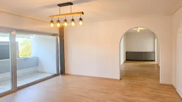 Helles Wohnzimmer mit Parkettboden, Zugang zum Balkon und einem modernen Deckenleuchter.