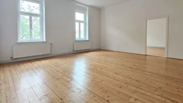 Helles, leeres Zimmer mit Holzdielenboden und zwei großen Fenstern, die viel Tageslicht hereinlassen.