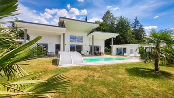 Moderne Villa mit großem Garten, privatem Pool und Palmen unter blauem Himmel.