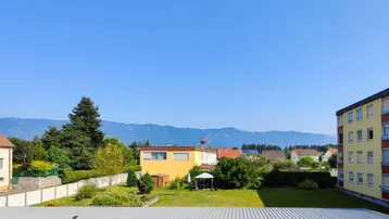 Weitläufiger Blick über einen Gartenbereich, Garagen und die umliegende Berglandschaft.