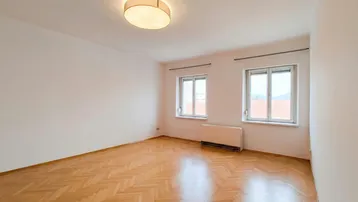 Helles Zimmer mit Fischgrätparkett und zwei Fenstern, ideal als Wohn- oder Schlafzimmer.