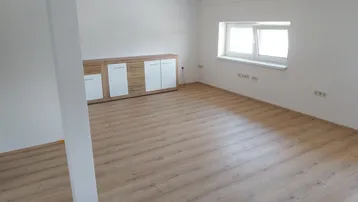 Heller, leerer Raum mit Laminatboden, weißen Wänden und einem Fenster, bereit zur Einrichtung.