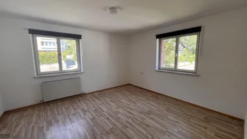 Helles Zimmer mit Laminatboden und zwei Fenstern, die viel Tageslicht hereinlassen.
