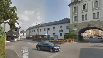 Straßenansicht mit Gebäuden, einem Auto und einem historischen Torbogen in einer städtischen Umgebung.