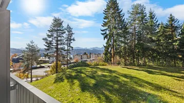Heller Balkon mit weitem Blick über grüne Hügel, Bäume und entfernte Berge unter blauem Himmel.