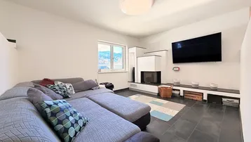 Gemütliches Wohnzimmer mit großem Ecksofa, modernem Kamin und dunklem Fliesenboden.