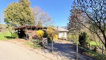 Zufahrt zum Anwesen mit Holzzaun, Carport und dem Haupthaus im Hintergrund.