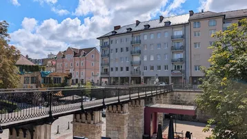 Städtische Ansicht mit Gebäuden, einer Brücke und Außenbereichen unter blauem Himmel.