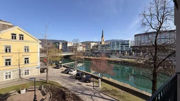 Panoramablick über den Fluss und die Stadt mit historischen Gebäuden und Bergen im Hintergrund, genossen von einem Balkon.