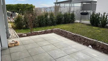 Gepflasterte Terrasse mit Rasenfläche und Hecken, ideal für entspannte Stunden im Freien.
