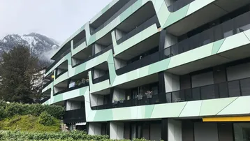 Moderne Wohnanlage mit auffälliger grüner Fassade, Balkonen und Bergblick im Hintergrund.
