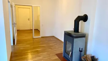 Helles Wohnzimmer mit modernem Kaminofen und Parkettboden, der zu weiteren Räumen führt.