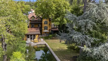 Luftaufnahme der Villa mit großem Garten, Teich und altem Baumbestand.