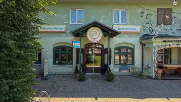 Vorderansicht eines Reformhauses und Naturkostladens mit grün gestrichener Fassade und gepflastertem Eingangsbereich.