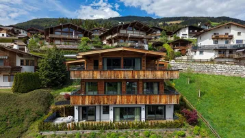 Modernes Chalet mit Holzfassade und mehreren Balkonen, eingebettet in eine grüne Hanglage.