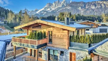 Modernes Chalet mit Holzfassade und Steinelementen vor beeindruckender Bergkulisse an einem sonnigen Tag.