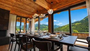 Geräumiger Essbereich mit Holzbalkendecke, großem Esstisch und Panoramafenstern mit Bergblick.
