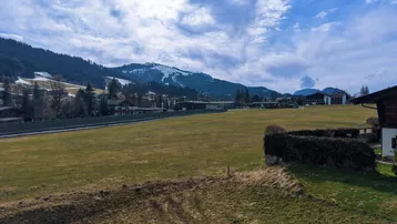 Weitläufige grüne Wiesen mit einem Zaun und schneebedeckten Bergen in der Ferne unter blauem Himmel.