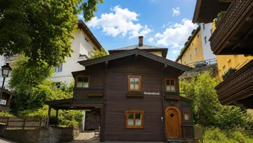 Traditionelles Holzhaus im Chalet-Stil mit dunkler Fassade und grünen Akzenten unter blauem Himmel.