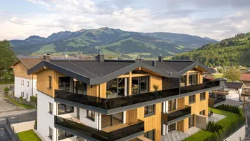 Modernes Apartmentgebäude mit Holzfassade, Balkonen und Bergblick in einer grünen Umgebung.