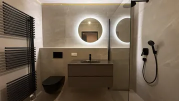 Modernes Badezimmer mit begehbarer Dusche, schwebendem Waschtisch und beheiztem Handtuchhalter in Grautönen.