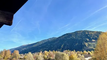 Panoramablick auf die umliegenden Berge und herbstliche Natur von einem Balkon aus.