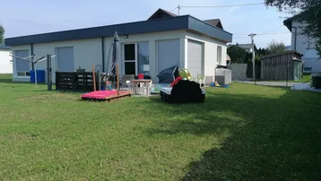 Großer Gartenbereich mit Rasenfläche, Spielgeräten und einer kleinen Terrasse am Haus.